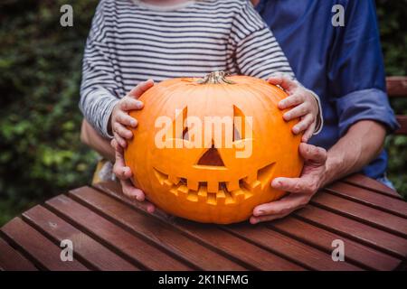 Vater und Tochter halten einen Kürbis für Halloween draußen. Hände. Frohe Familie Stockfoto