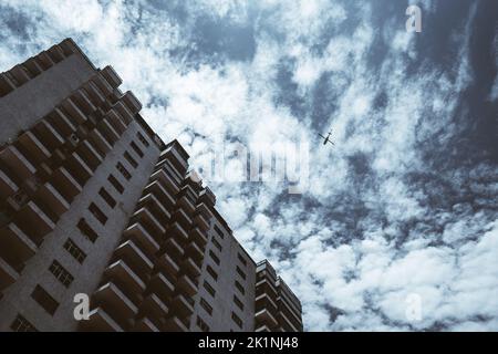 Blick vom unteren Ende einer Wohnhaushöhe mit vielen Balkonen und Fenstern, wunderschöner blauer Himmel mit Wolkenlandschaft und der Silhou Stockfoto