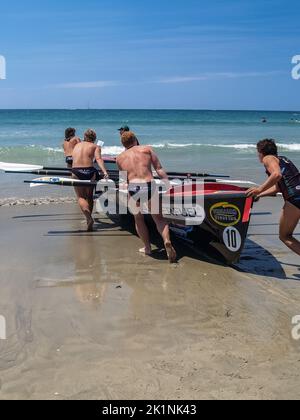 Tauranga, Neuseeland - Januar 25 2009; eine Gruppe konkurrierender Surf-Rettungsschwimmer schiebt das Surfboot ins Meer. Stockfoto