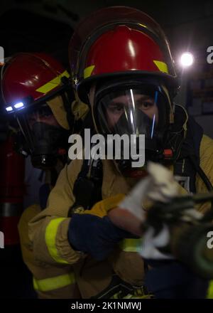 220919-N-VJ326-1225 PHILIPPINISCHES MEER (SEPT 19, 2022) – Damage Controlman Fireman Joseph Leitner, aus Bemidji, Minnesota, Right, and Damage Controlman 3. Class Chandler Peters, aus Uhrichsville, Ohio, Kämpfe während des Damage Control Trainings an Bord des amphibischen Angriffsträgers USS Tripoli (LHA 7) am 19. September 2022 gegen ein simuliertes Feuer. Tripolis ist im Einsatzgebiet der US-Flotte von 7. tätig, um die Interoperabilität mit Verbündeten und Partnern zu verbessern und als einsatzbereite Einsatztruppe für den Frieden und die Stabilität in der Region Indo-Pazifik zu dienen. (USA Navy Foto von Mass Communication Specialist 2. CL Stockfoto