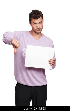 Ich stimme nicht zu... Ein hübscher Mann, der ein leeres Plakat vor einem weißen Hintergrund hält und einen Daumen nach unten zeigt. Stockfoto