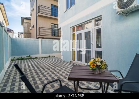 Außenansicht des Hinterhofs Moderne Villa oder Wohngebäude mit Tisch und Stühlen auf der Terrasse und Zaun. Stockfoto