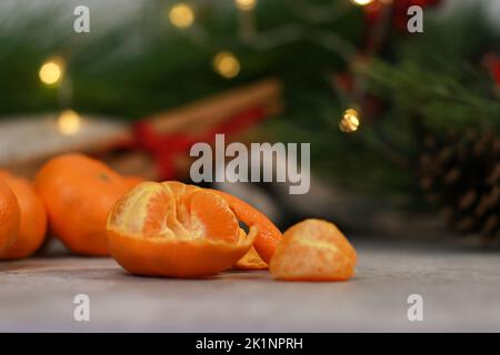 Nahaufnahme einer geschälten Mandarine, verschwommener Hintergrund mit Weihnachtsbaum und Lichtern Stockfoto
