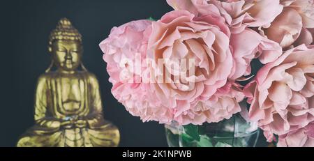 Ein Strauß rosa Rosen und eine Statue von goldenem Buddha im Hintergrund Stockfoto