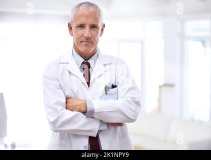 Ihre Gesundheit ist meine oberste Priorität. Porträt eines reifen Arztes, der mit gekreuzten Armen steht. Stockfoto