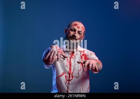 Portrait eines Mann-Zombies mit Kratzern und finsteren Wunden vor der Kamera, gefährlicher untoter Leiche mit gruseligen Narben und gruseligem Gesicht im Studio. Weltuntergang grausamer Monsterteufel. Stockfoto