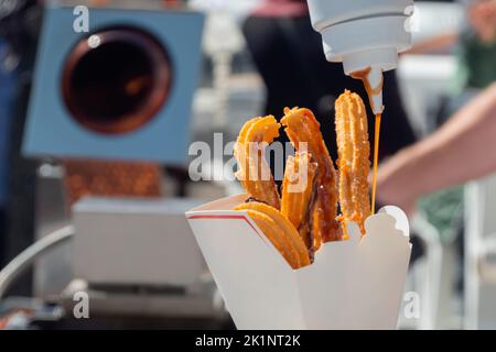 Frau goss Karamellsauce auf hausgemachten knusprigen Churros in einer Papierbox - Nahaufnahme Stockfoto