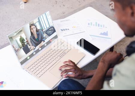 Ein vielseitiger Geschäftsmann mit Papieren und Telefonaten am Schreibtisch, der mit weiblichen Kollegen während eines Videoanrufs diskutiert Stockfoto