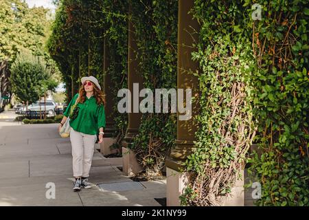 Junge Frau, die auf der Straße läuft und einen Netzbeutel mit Gemüse auf der Schulter hält. Nachhaltiges Einkaufen, moderner Lifestyle Stockfoto