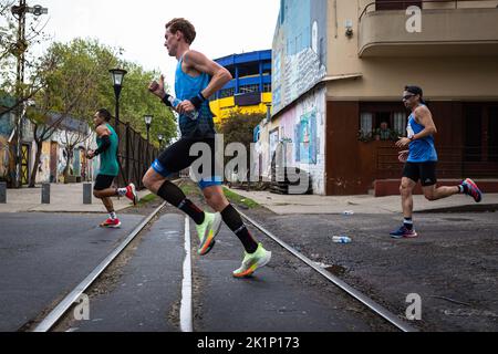 Buenos Aires, Argentinien. 18. September 2022. Drei Elite-Läufer überqueren einige Bahngleise im Viertel La Boca in Buenos Aires. Hinter den blauen und gelben Farben können Sie das Fußballstadion des Club Boca Juniors sehen. Neuntausend Menschen füllten die Straßen der Stadt während des Buenos Aires-Marathons 42K. Mit mehr als 1.600 ausländischen Läufern, darunter viele aus Brasilien, Uruguay und Chile, konnte der internationale Wettbewerb seinen ganzen Glanz zurückgewinnen. (Foto von Nacho Boullosa/SOPA Images/Sipa USA) Quelle: SIPA USA/Alamy Live News Stockfoto