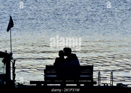 Eine Silhouette eines Paares, das auf einem Sitzplatz am Ende eines Bootsanlegeplatzes romantisch ist. Stockfoto