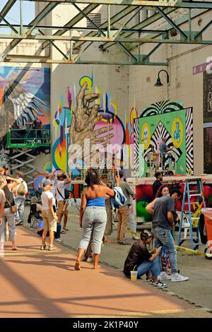 Beim RVA Street Art Festival im Kraftwerk entlang des Canal Walk von Richmond VA beobachten Besucher die Entstehung neuer Wandgemälde. Stockfoto