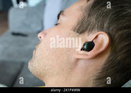 Junger Mann hört Musik, die auf der Couch liegt. Konzepte der Tagesruhe und des Musikhörens. Schlafen Sie mit Musik. Stockfoto