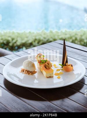 Kokoseis-Dessert und Mangokuchen auf einem Teller am Pool. Tropisches Dessert Stockfoto