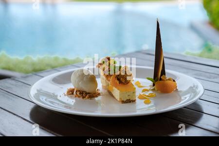 Kokoseis-Dessert und Mangokuchen auf einem Teller am Pool. Tropisches Dessert Stockfoto