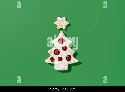 Oben mit einem Keks in Form eines weihnachtsbaums und einem Stern. Leckere linzer-Kekse mit Himbeermarmelade, minimalistisch auf einem grünen Tisch. Stockfoto