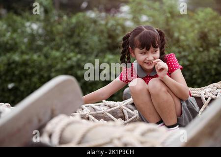 Fröhliches Mädchen, das auf einem Drahtseil auf einem Spielplatz spielt. Stockfoto