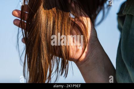 Die Frau greift nach ihren glänzenden Haaren. Nahaufnahme der Hand, die die Haare hält. Kämmen mit Pinsel und zieht lange Haare. Tägliche Vorbereitung auf das Aussehen schön. Haarausfall Stockfoto