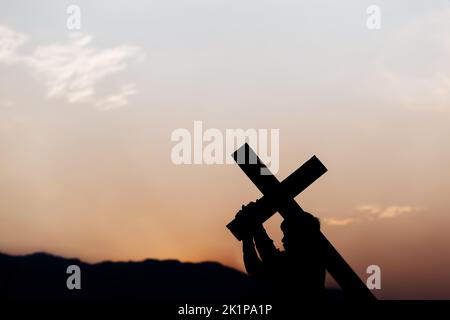 Silhouette eines Mannes, der bei Sonnenuntergang ein Kreuz trägt. Begriff der Religion. Stockfoto