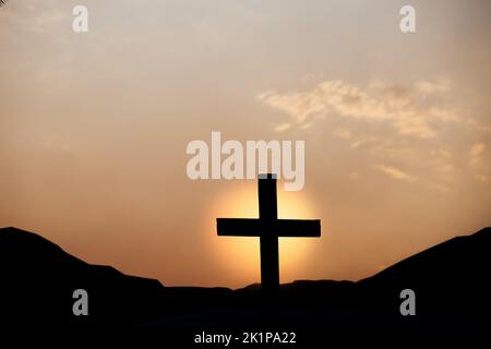 Silhouette des Kreuzes auf dem Berg bei Sonnenuntergang. Begriff der Religion. Stockfoto