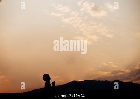 Silhouette eines Mannes Gebet auf Berg bei Sonnenuntergang. Begriff der Religion. Stockfoto