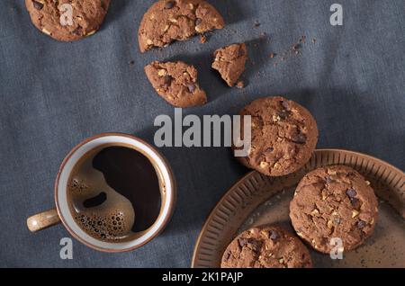 Chocolate Chip Cookies neben einer Tasse Kaffee auf Stoffhintergrund, Draufsicht Stockfoto