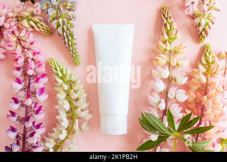 Weiße Squeeze Bottle Tube für Branding von Medizin oder Kosmetik - Creme, Gel, Hautpflege, Feuchtigkeitscreme. Kosmetische leere Flasche Mockup und rosa Lupine Flow Stockfoto