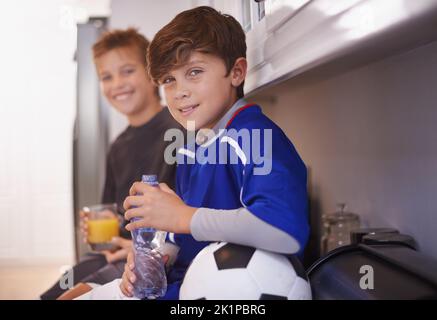 Die Jungen werden Jungen sein. Zwei junge Jungen, die nach dem Fußballtraining kalte Getränke trinken. Stockfoto