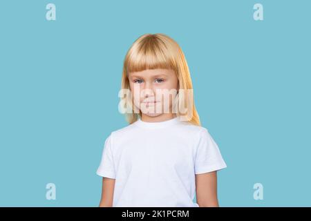 Sarkastisches Kind. Freche Kindheit. Unschuldige Schönheit. Porträt von schüchtern verwirrt niedlich blonde kleine Mädchen in weißem T-Shirt Blick auf Kamera isoliert auf blu Stockfoto