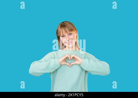 Unterstützende Frau. Romantische Botschaft. Liebe Fürsorge. Bewunderung. Porträt einer fröhlichen Dame im Pullover, die eine Herzgeste zeigt, die isoliert lächelt Stockfoto