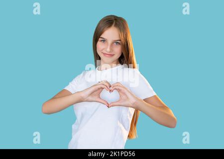 Unterstützender Teenager. Liebe Fürsorge. Bewunderung, Mitgefühl. Portrait von fröhlichen Mädchen in weißem T-Shirt zeigt Herz Geste lächelnd isoliert auf blau Stockfoto