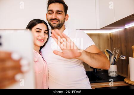 Ein junges Paar, das zu Hause in einer Küche sitzt und mit seiner Familie telefoniert. Sie sehen sehr glücklich aus. Stockfoto