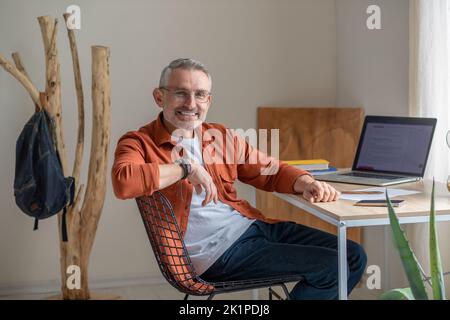 Ein bärtiger reifer Mann, der im Büro am Tisch sitzt Stockfoto