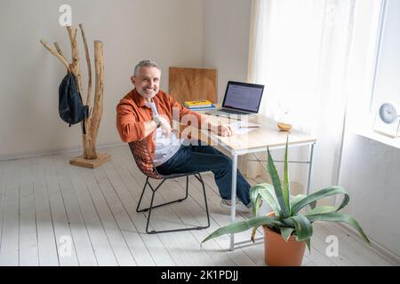 Ein bärtiger reifer Mann, der im Büro am Tisch sitzt Stockfoto