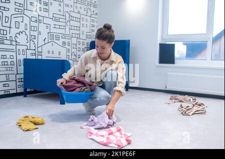 Hausfrau sammelt verstreute Kleidung in die Waschschüssel Stockfoto