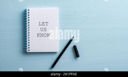 Lassen Sie uns wissen, Zeichen in Spiralnotizbuch mit einem schwarzen Marker daneben auf blauem Holzhintergrund geschrieben. Stockfoto