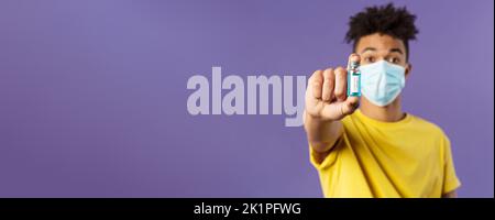 Medizin, Coronavirus und Menschen Konzept. Nahaufnahme des jungen Mannes in der Gesichtsmaske, die Ampulle mit dem Medikament hält, schließlich Impfstoff aus Kovid19 gefunden Stockfoto