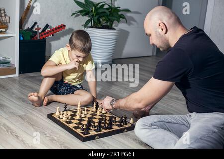 Vater und Sohn spielen Schach auf dem Boden im Kinderzimmer unter den Spielzeugen. Stockfoto