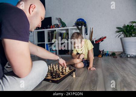 Vater und Sohn spielen Schach auf dem Boden im Kinderzimmer unter den Spielzeugen. Stockfoto