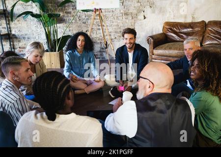 Ein multirassisches kreatives Marketingteam aus jungen Menschen und Erwachsenen, die auf dem Boden sitzen, traf sich zum Brainstorming und zur Planung eines Projekts oder einer Suche Stockfoto
