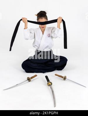 Aikido-Meisterin im traditionellen Samurai-Hakama-Kimono mit schwarzem Gürtel mit Schwert, Katana auf weißem Hintergrund. Gesundes Lifestyle- und Sportkonzept. Stockfoto