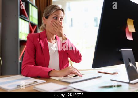 Geschäftsfrau schaut überrascht auf den Bildschirm und bedeckt den Mund mit der Hand Stockfoto