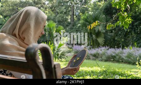 Muslim Women genießt ihre Stickarbeit auf der Bank im Park Stockfoto