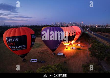 Eine Gruppe farbenfroher Heißluftballons füllt sich, um bei Sonnenuntergang in Melbourne abzuheben Stockfoto