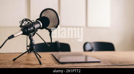 Standbild eines Mikrofons mit einem Pop-Schild, das auf einem Tisch neben einem digitalen Tablet platziert ist. Podcast-Aufnahmeset in einem Heimstudio. Stockfoto