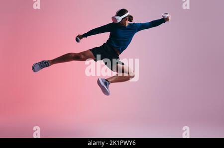 Junger Mann, der Kampfkunst in virtueller Realität übt. Sportlicher junger Mann, der einen Kick in der Luft wirft, während er ein Virtual-Reality-Headset trägt. Aktive junge m Stockfoto