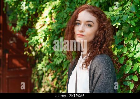 Portrait junge zarte rothaarige junge Mädchen mit gesunder Sommersprossen Haut in weißem Hemd und grau Blick auf die Kamera mit nachdenklichen Ausdruck. Kaukasische Frau Modell mit Ingwer Haar posiert im Freien Stockfoto