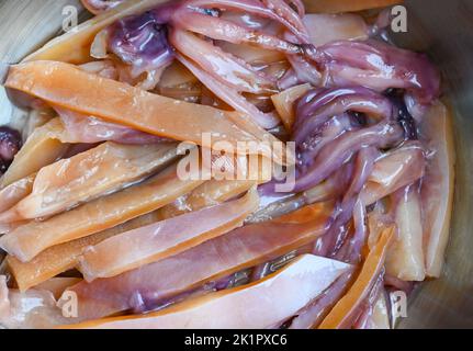 Roher Tintenfisch zum Kochen von Speisen auf einem Holztisch, Konservierung von Fisch und Meeresfrüchten, eingelegter Tintenfisch auf einer Schüssel Stockfoto