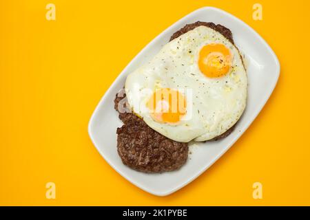 Drei gebratenes Hackfleisch mit Spiegelei auf weißem Teller auf Gelb Stockfoto