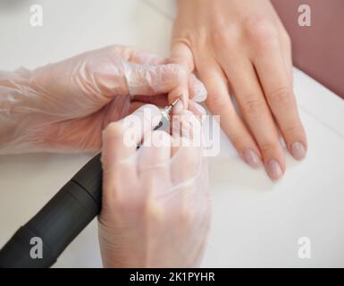 Maniküre Master mit Nagelhautentferner Gerät während der Durchführung Hardware Maniküre im Schönheitssalon. Nahaufnahme einer weiblichen Manikuristin in sterilen Handschuhen, die mit einem elektrischen Nagelbohrer die Nagelhaut an der Hand einer Frau entfernt Stockfoto